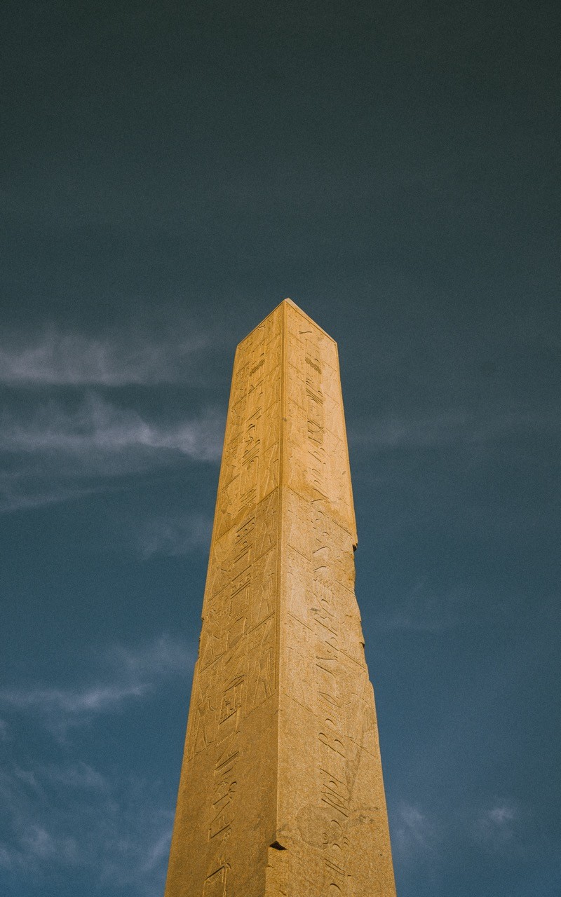 The obelisk of Hatshepsut rising above the ruins of the Karnak Temple against a clear sky.