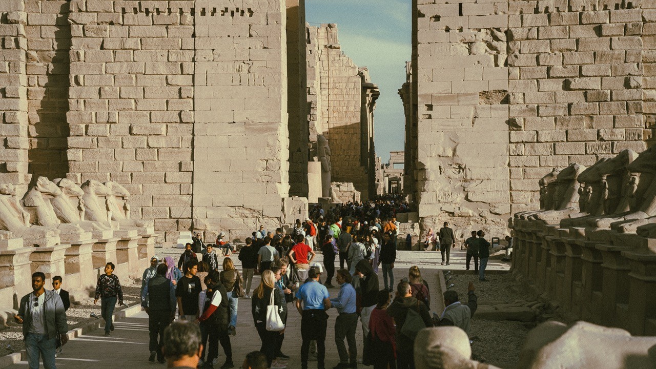 Tourists gathered at the entrance of the Karnak Temple, dwarfed by the towering stone walls.