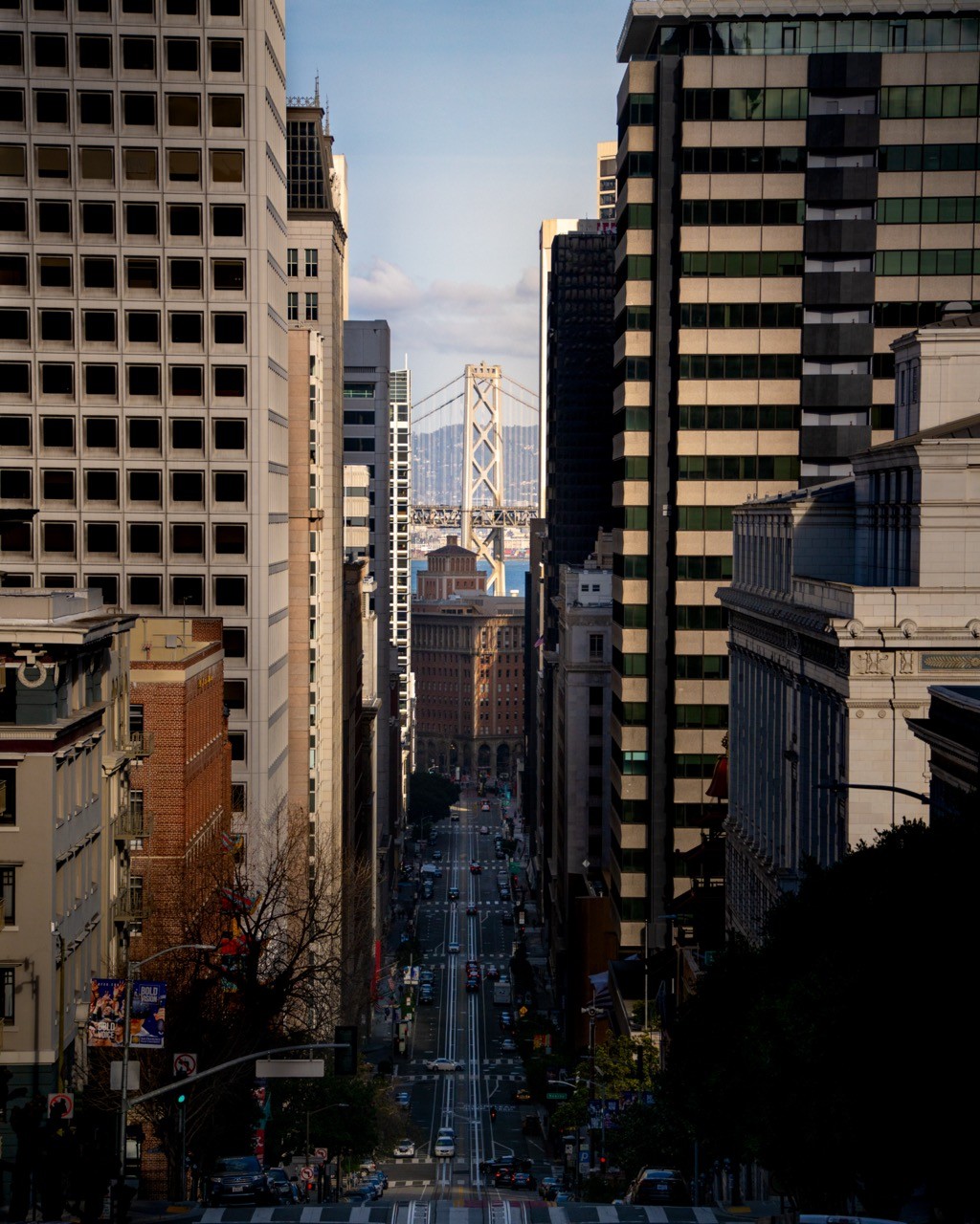 The Bay Bridge centered at the end of a San Francisco street, framed by buildings on either side.