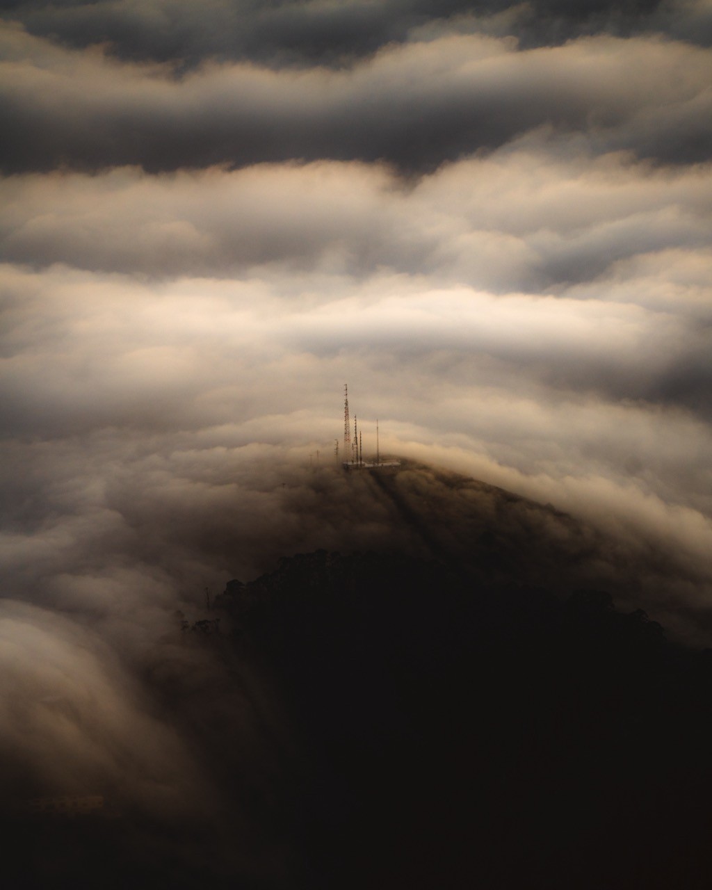 Radio towers poking out of a glowing fog line at sunset, reminiscent of Howl's Moving Castle.