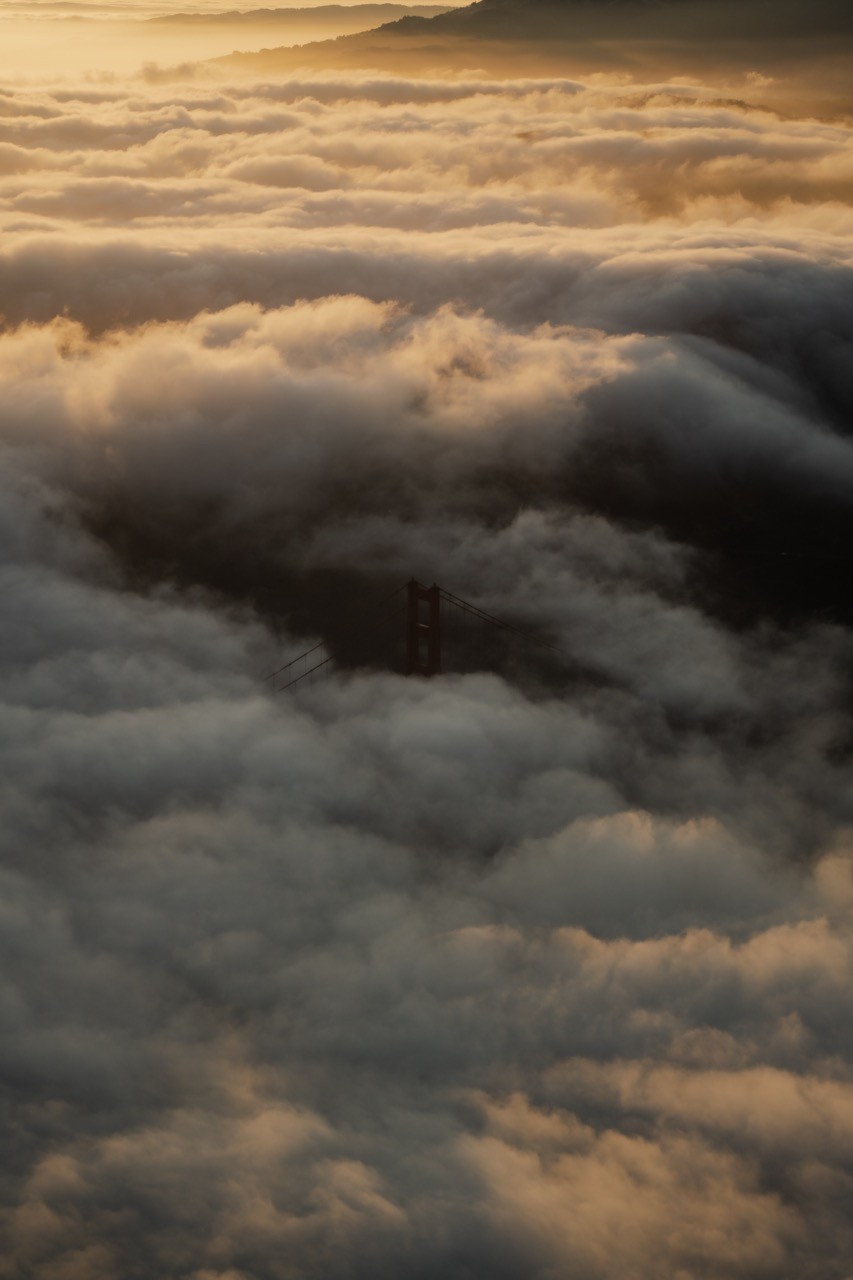 The Golden Gate Bridge barely peeking out from a rolling fog line at sunset.