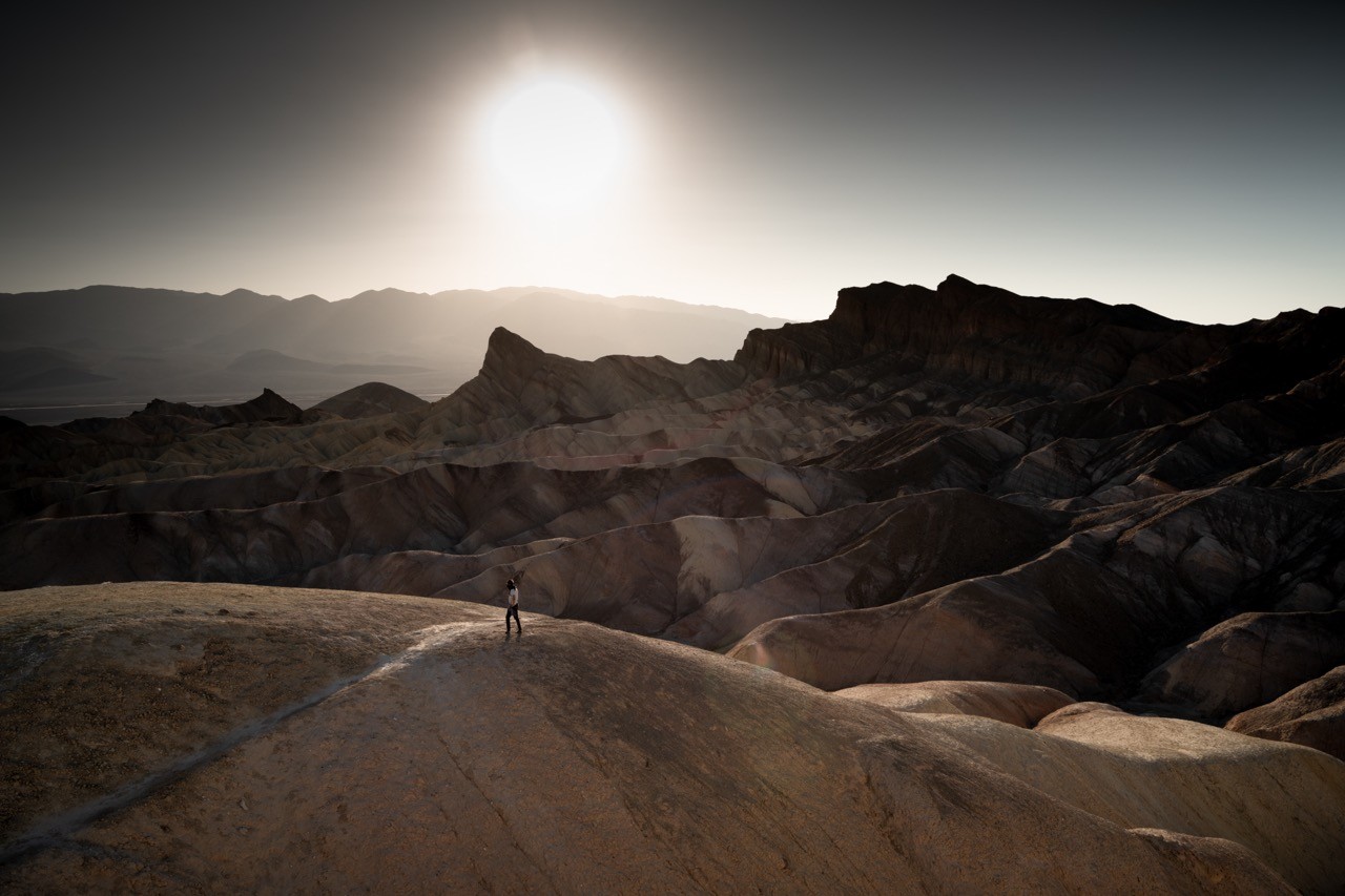 A lone figure at Zabriskie Point looking into the sun over the scorched desert landscape.